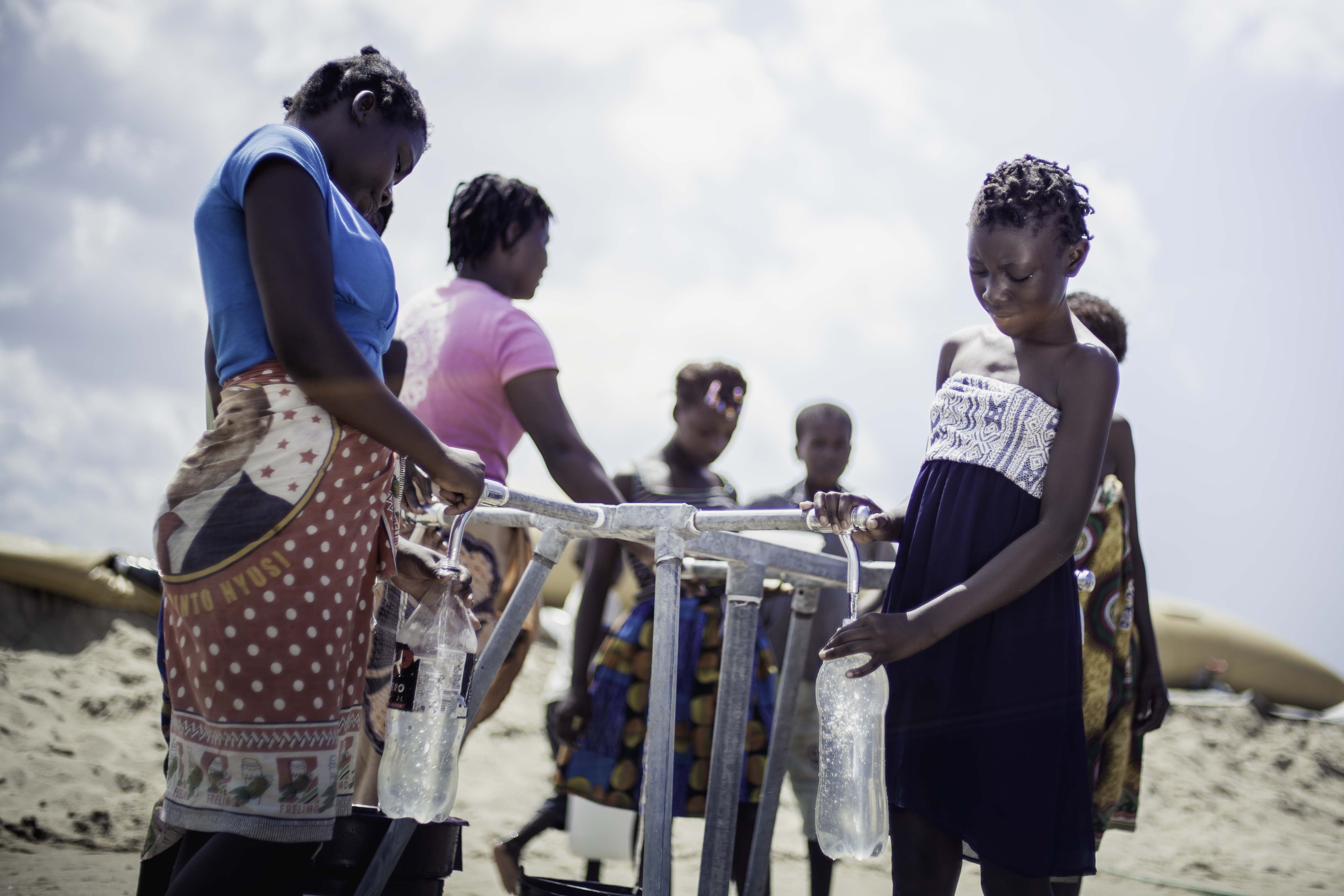 14岁的Teresa Jone Vilanculos（右）从水龙头取水，注满自己的瓶子。 Teresa和她的家人原本居住在莫桑比克的Mangalaforte。因为房子被「伊代」摧毁，她全家被迫要逃往临时庇护中心暂住。（摄影： Micas Mondlane / 荷兰乐施会）